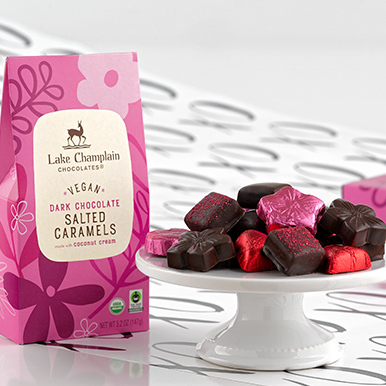 Vegan salted caramel flower gift box sitting next to a white ceramic dish with assorted vegan chocolates.