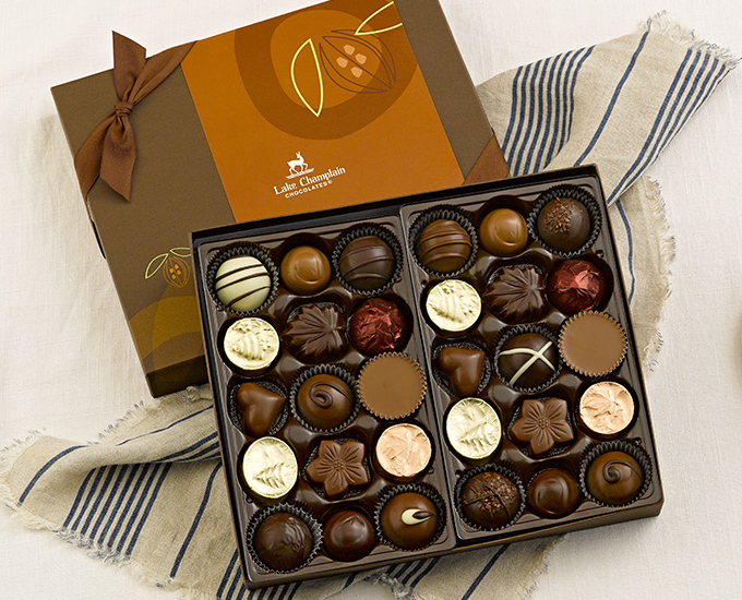 30 pieces of assorted gourmet chocolates in a brown gift box with a brown ribbon on the cover of the gift box, sitting on a cream napkin with blue stripes.