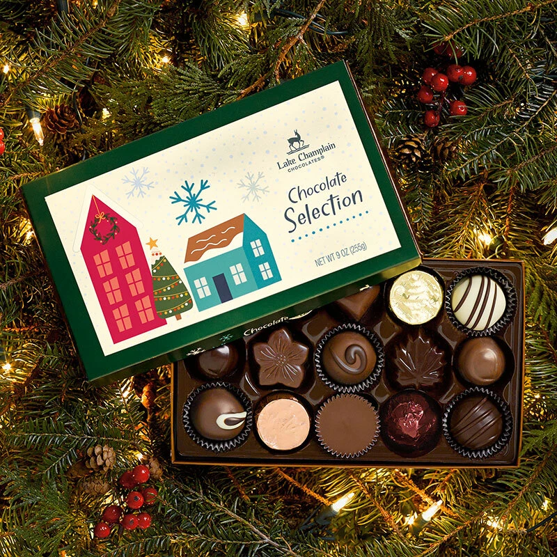 15 piece holiday selection box filled with assorted gourmet chocolates sitting on Christmas greens with berries, pinecones, and white Christmas lights.