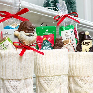 Assorted Christmas  chocolates in white knitted stockings, hanging on metal hangers on a white fireplace mantel.