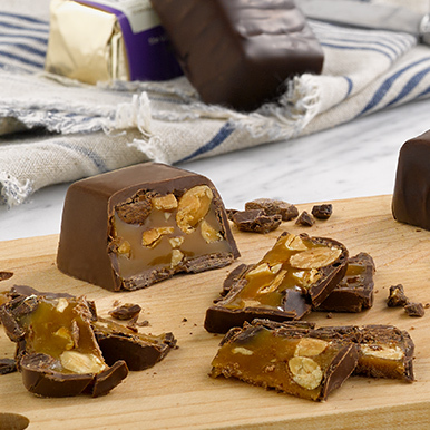 Milk chocolate caramel five star bar  unwrapped and cut up on a wooden cutting board, sitting on white marble with a white and blue stripped napkin in the background.