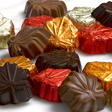 Assorted milk and dark chocolate leaves wrapped in orange, red and gold foils and unwrapped leaves in a pile.