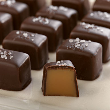 Dark chocolate sea salt caramels lined up  in rows with one of the front sea salt caramels cut in half