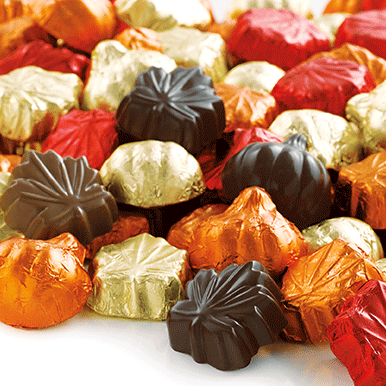 A bunch of assorted milk and dark chocolate leaves and pumpkins sitting on a white surface.