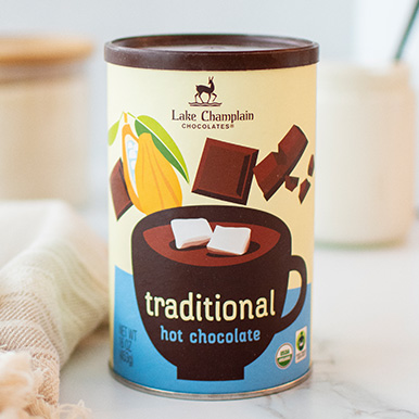 Tin of organic and fair trade gourmet traditional hot chocolate on a marble counter next to an off white table cloth.