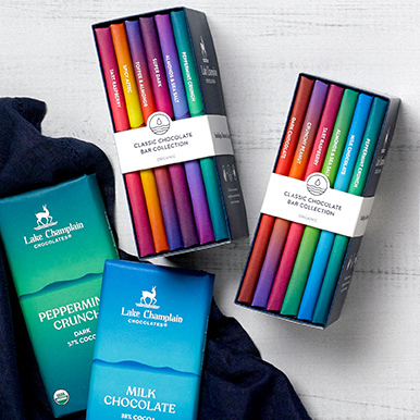 Two assorted chocolate bar libraries sitting on a wooden surface with a dark navy blue napkin on the left side of the libraries with two chocolate bars sitting on the napkin.