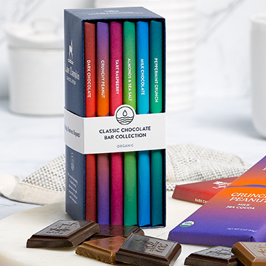 Assorted chocolate bar library  sitting on a round white marble dish with unwrapped pieces of chocolate around the library and wrapped bars on the side.