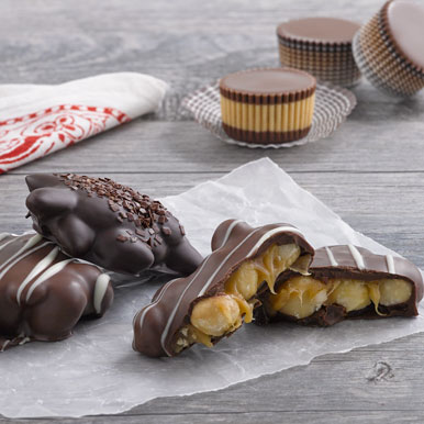 Assorted milk and dark chocolate caramel nut clusters and milk chocolate peanut butter cups on a gray wooden table with a white and red handkerchief in the left hand corner