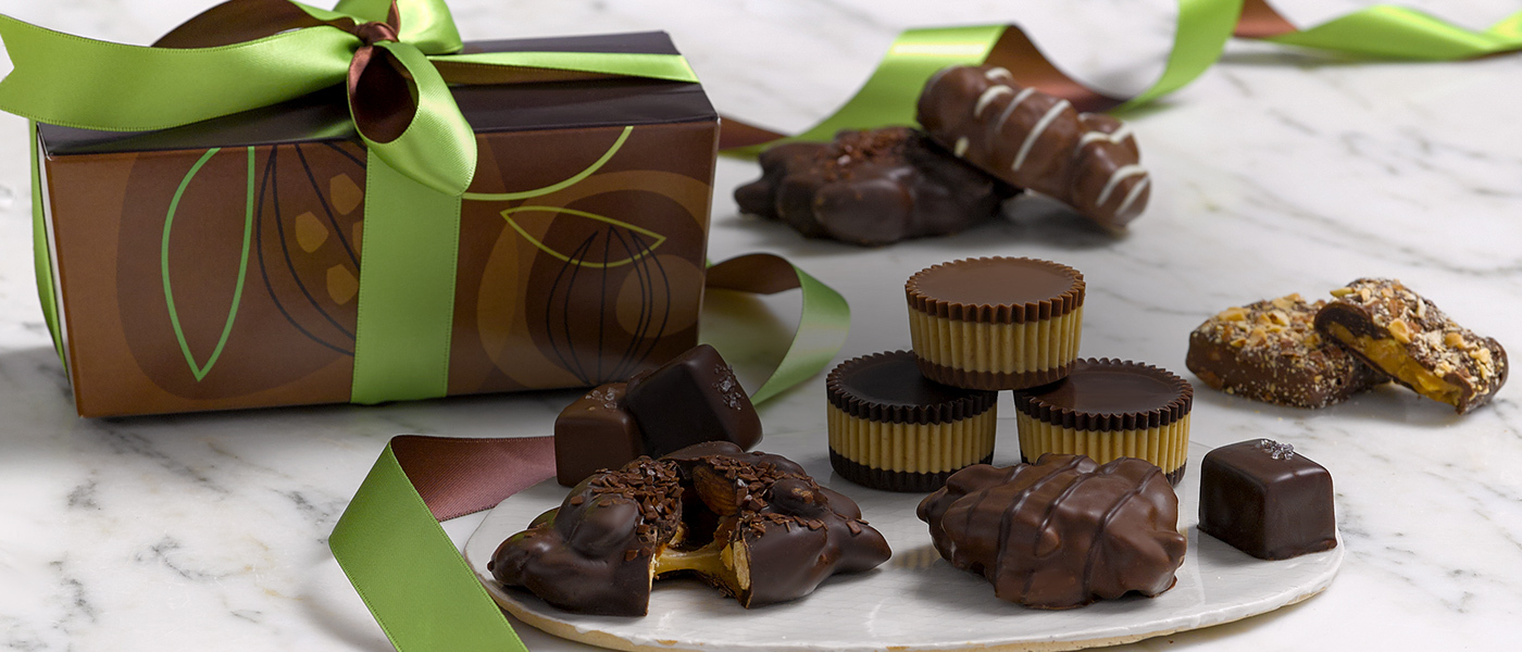 Dark chocolate almond clusters, dark chocolate peanut butter cups, a milk chocolate pecan caramel cluster, milk and dark sea salt caramels siting on a white, round marble plate with almond butter crunch, a pecan caramel cluster and maca