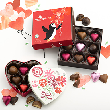 Assorted chocolate hearts and bonbons in Valentine's Day themed gift boxes with paper hearts in the background and wrapped and unwrapped chocolates around the gift boxes.