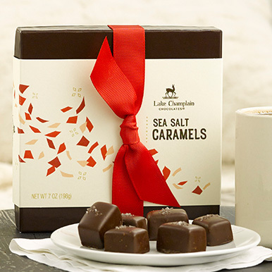 Milk chocolate sea salt caramels on a white plate with a gift box behind it and a cup of coffee next to it.