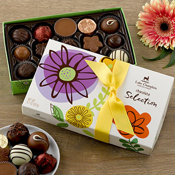 Assorted gourmet chocolates in a spring themed gift box with a small circular ceramic dish sitting next to it with assorted chocolates on it.