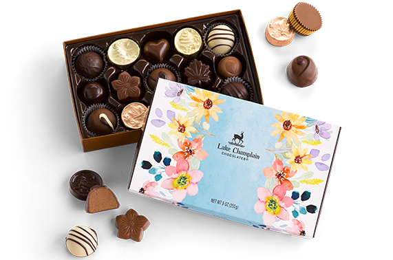 Assorted gourmet chocolates in a Spring themed gift box with unwrapped assorted chocolates around the box.