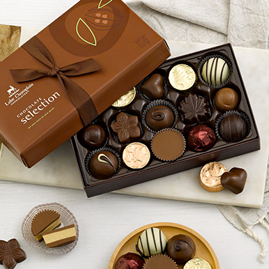 Assorted gourmet chocolates in a brown gift box, on a cutting board and in a gold dish.