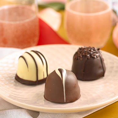 Assorted gourmet chocolate truffles on a  white ceramic plate with glasses of champagne in the background.