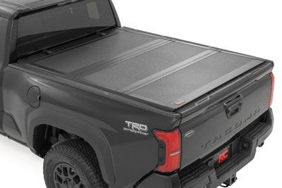 Elevate your Toyota's functionality and appearance with Rough Country's fourth-generation Tacoma Hard Tri-fold Flip-up Bed Cover. Unlike traditional bed covers that limit access to your truck bed, our innovative Flip-up design grants you complete access to your truck bed, making it easier to load and unload large items.Full-Bed Access: With Rough Country's Tri-fold Flip-up Bed Cover, you can conveniently flip up the cover, allowing full-bed access without the hassle of removing the cover.Built to Last: Our bed cover is crafted from lightweight aluminum and boasts a resilient powder coat finish. This coating resists corrosion and wear, ensuring that your truck bed maintains its pristine appearance even in harsh weather conditions.Superior Water Drainage System: The bed rails of this bed cover feature an innovative water drainage system. No need to worry about water pooling on your cover or seeping into your truck bed.Premium Weather Seals: The Tri-fold cover also includes top-of-the-line weather-resistant seals that create a tight and secure barrier along the bed rails. These seals ensure your cargo remains protected from the elements, even in inclement weather.Secure Cargo Storage: Provide added security for your truck bed contents, deterring theft and protecting valuable items.Elevate your TacomaΓÇÖs truck bed and get full access, unmatched durability, and superior weather protection with Rough Country's Hard Tri-fold Flip-up Bed Cover!