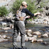 SJK Pursuit Hunting Vest in Kryptek Highlander camouflage on a fly fisherman casting a line into a stream.