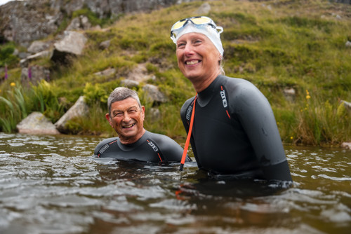 Two people in the lake wearing the ZONE3 Active-Flex, smiling with green fields behind them