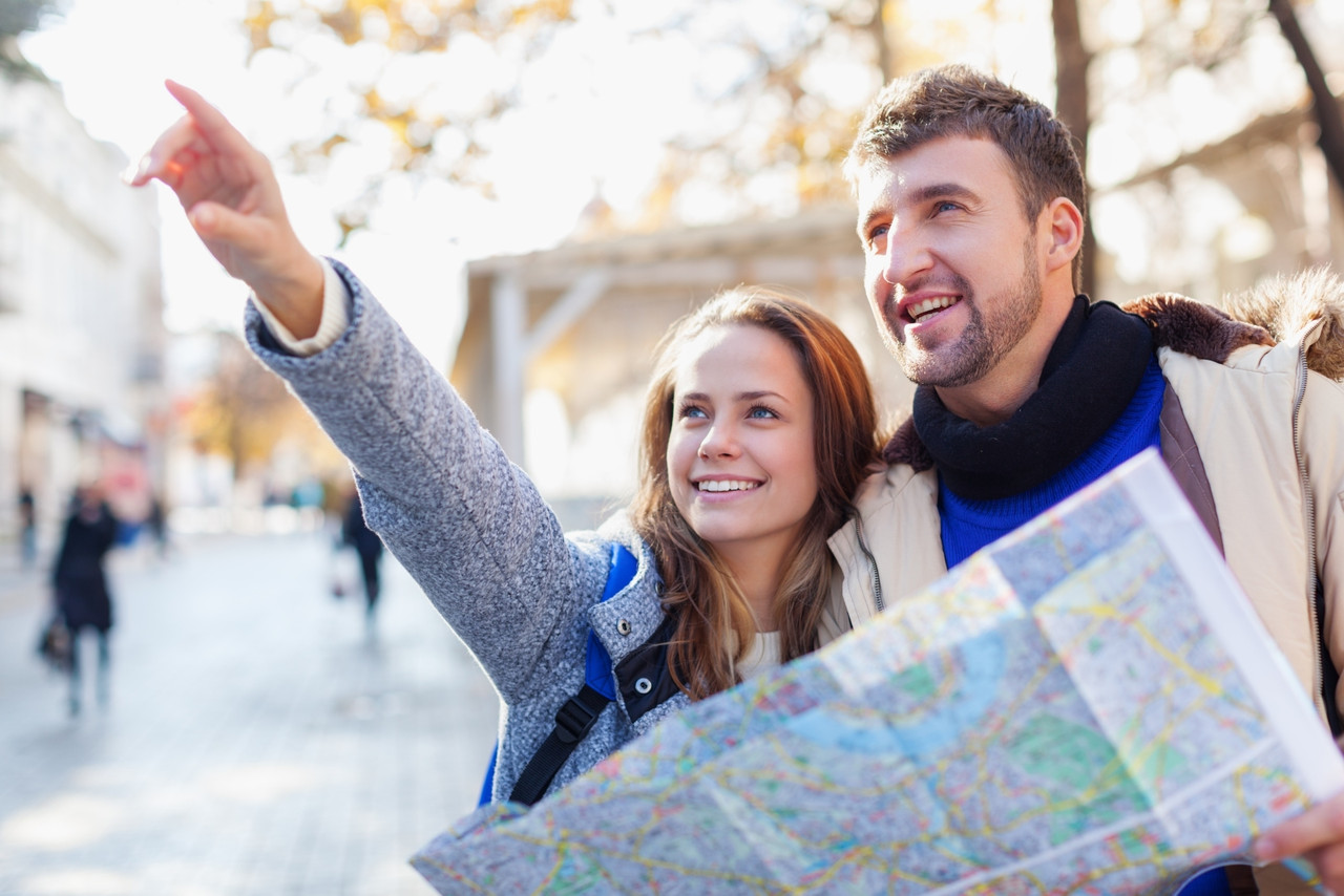 A male and female couple looks at something in the distance while holding a map during their travels