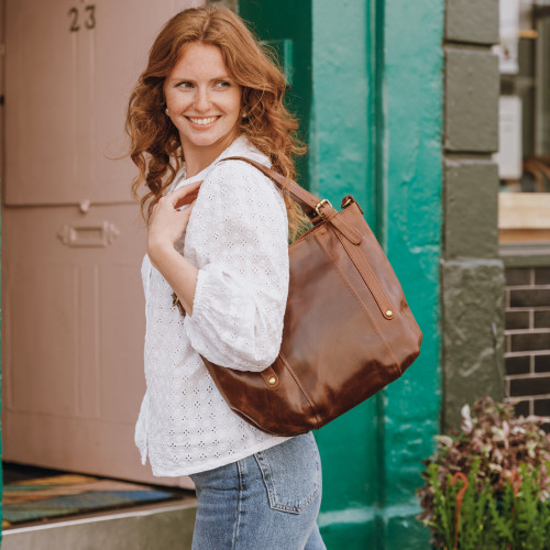 brown leather tote with adjustable handles worn over a woman's shoulder