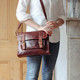brown oiled leather satchel with long shoulder strap, front pocket and buckle fasteners, worn on model