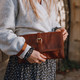 tan leather clutch bag with a detachable wrist strap and buckle feature, held by model