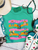 Bright, bold, and full of western spirit, our Life of a Cowboy Vibrant Graphic Tee celebrates the grit, tradition, and excitement of cowboy life. Featuring colorful hand-drawn rodeo scenes—including bronc riding, roping, ranch work, fencing, and western tack—this eye-catching design is finished with playful retro-inspired stripes that make it a true statement piece.
Printed on your choice of Softstyle, Comfort Colors, or a Muscle Tank, this tee is incredibly soft and perfect for rodeos, county fairs, livestock shows, country concerts, or everyday western style. Whether you grew up in the arena or simply love the western way of life, this shirt brings cowboy culture to life with a fun, artistic twist.