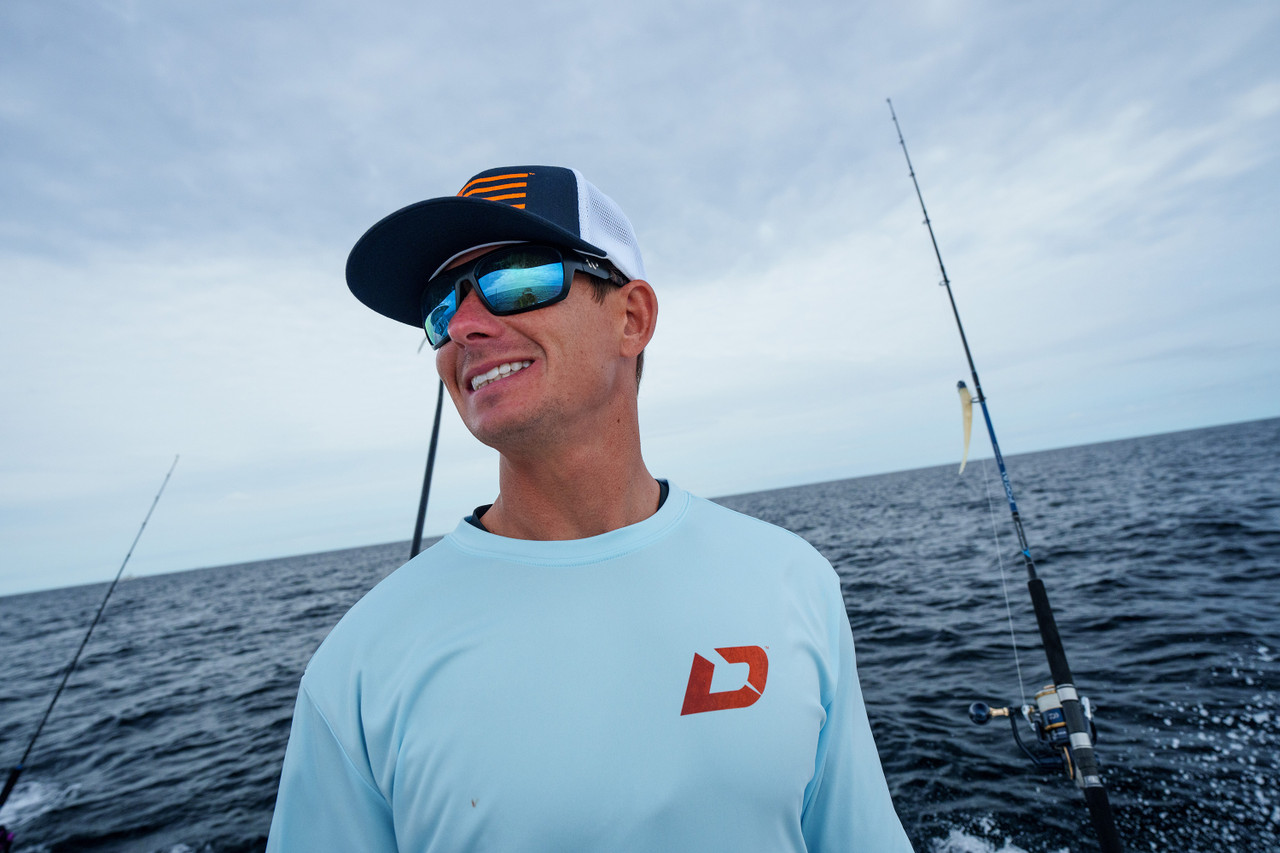 Man in Purple Shirt and Orange Cap Holding Fishing Rod Near Sea