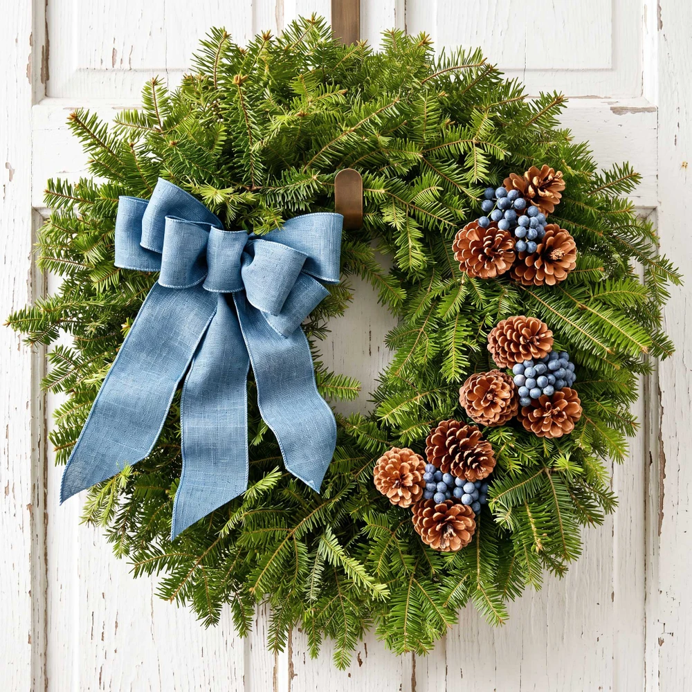 Front view of the Bar Harbor fresh Maine balsam wreath with a blue linen bow and blueberries centered on a white rustic door.