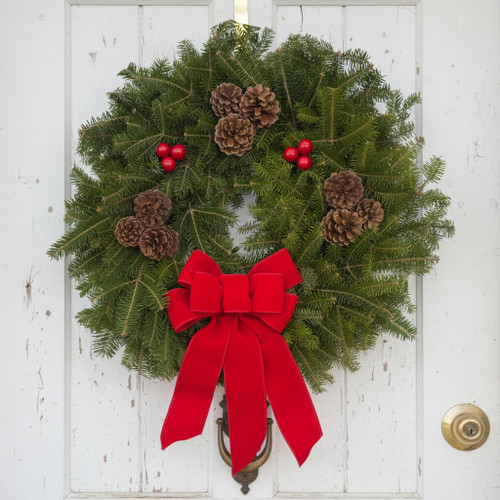 Close-up of a handmade Downeaster fresh Maine balsam wreath showcasing the lush needles and vibrant red berry clusters against white wood.