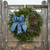A fresh Bar Harbor balsam wreath with blue ribbon hanging on a rustic wire and wood farm gate.