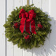 A fresh Acadia balsam wreath with a red velvet bow hanging on a white farmhouse-style door, creating a classic New England holiday entryway in golden hour.