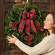 Woman beside a Country Plaid fresh balsam wreath with tartan bow on a dark wood door