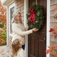 Woman and child hanging a Winterberry fresh balsam Christmas wreath on a dark wood front door