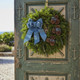 A fresh Bar Harbor balsam wreath with a blue ribbon displayed on a rustic green door decorated with nautical anchor symbols.