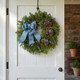 A fresh Bar Harbor balsam wreath with blue linen ribbon and blueberries hanging on a clean white interior door.