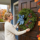 Woman hanging a Bar Harbor fresh balsam wreath with blue linen bow, pinecones and blueberries on a front door