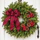 Buffalo Plaid fresh Maine balsam Christmas wreath with pinecones, red berries and red-and-black plaid bow on a white wooden door