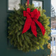 Classic balsam Christmas wreath with red velvet bow on a green front door in winter
