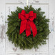 A close-up view of the Classic Maine balsam wreath with a red velvet bow hanging on a white, weathered farmhouse door.
