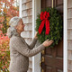 Woman hanging a fresh balsam Christmas wreath with red velvet bow on her front door