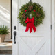An old-fashioned Downeaster balsam wreath with large red berry clusters and pinecones displayed on a white rustic barn door.