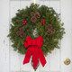 Close-up of a handmade Downeaster fresh Maine balsam wreath showcasing the lush needles and vibrant red berry clusters against white wood.