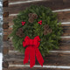 A lush Downeaster fresh Maine balsam wreath with an old-fashioned bottom bow hanging on a weathered log cabin wall.