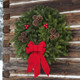 A lush Downeaster fresh Maine balsam wreath with an old-fashioned bottom bow hanging on a weathered log cabin wall.