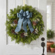 The elegant Blueberry fresh Maine balsam wreath with a blue linen bow and white statice displayed on a clean white rustic door in a bright home entryway.