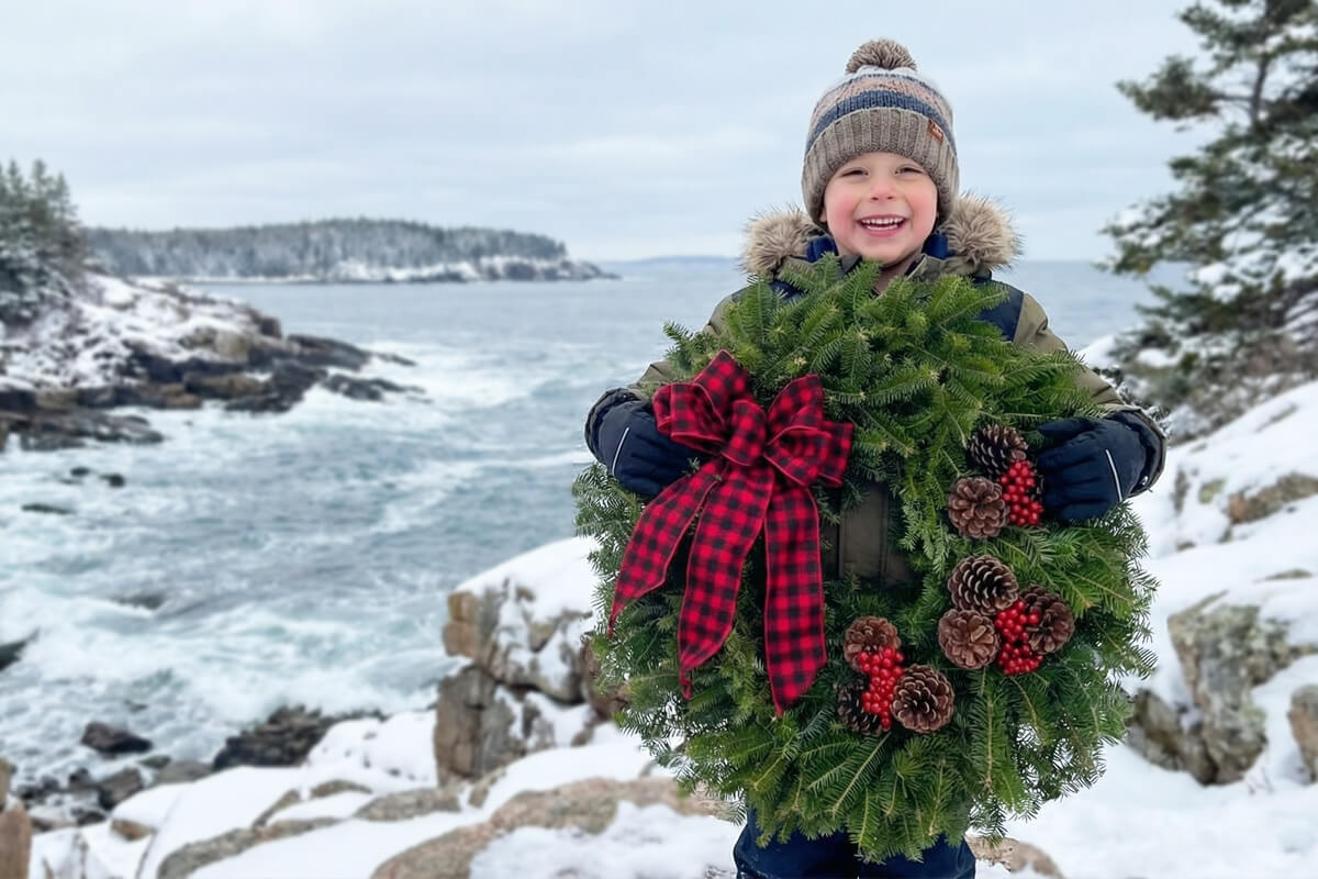 Handcrafted Buffalo Plaid Fresh Maine Balsam Wreath held by boy on rocky coast