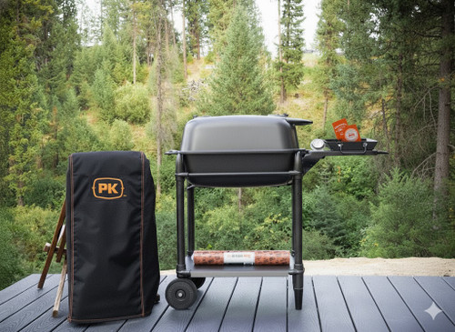 PK Grills PK300 Start Cookin' Bundle - Graphite, outdoor portable grill setup with cover and accessories on a wooden deck with a lush green forest background.