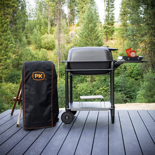 PK Grills PK300 Start Cookin' Bundle - Graphite, outdoor portable charcoal grill with accessories on a wooden deck, surrounded by a lush green forest.