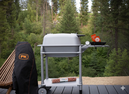 PK Grills PK300 Start Cookin' Bundle - Silver, outdoor grill with accessories, set up on a deck with a view of a green forest.